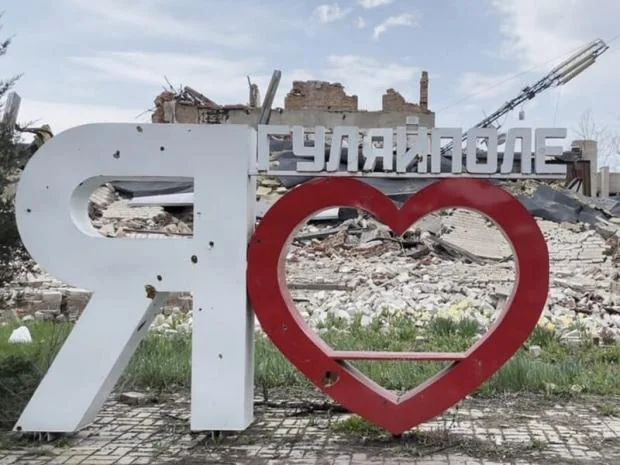 Зруйнований знак «Гуляйполе» з серцем на тлі руїн міста