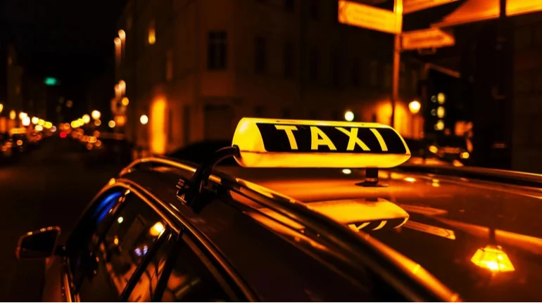Жовтий ліхтар таксі з написом TAXI на даху авто в нічному місті