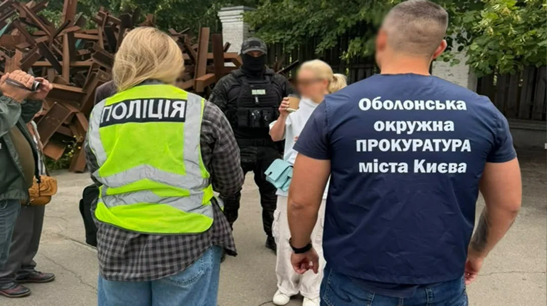 Правоохоронці в жилетах поліції та прокуратури біля озброєного чоловіка в масці